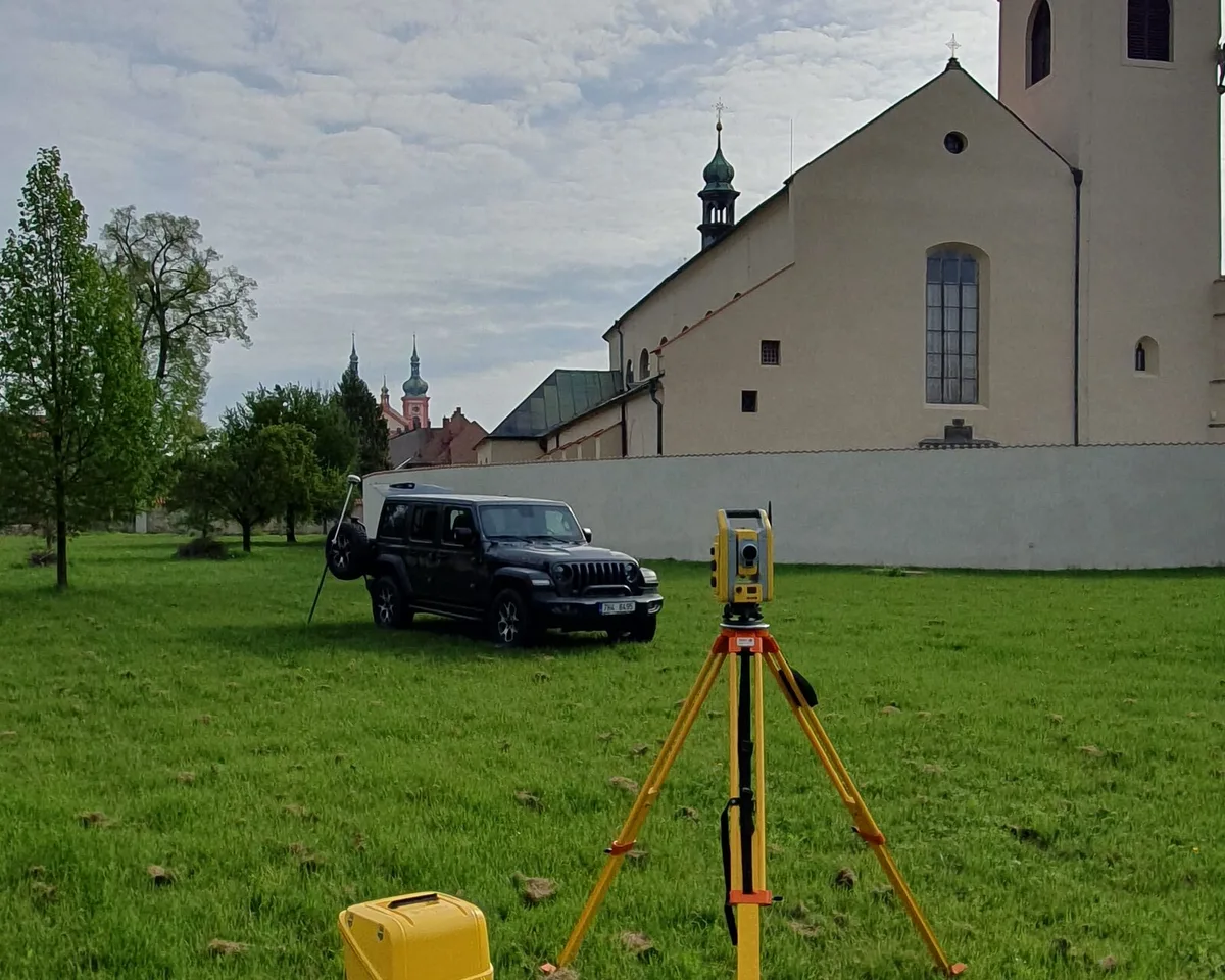 Totální stanice na stativu a terénní vůz geodeta na louce před kostelem